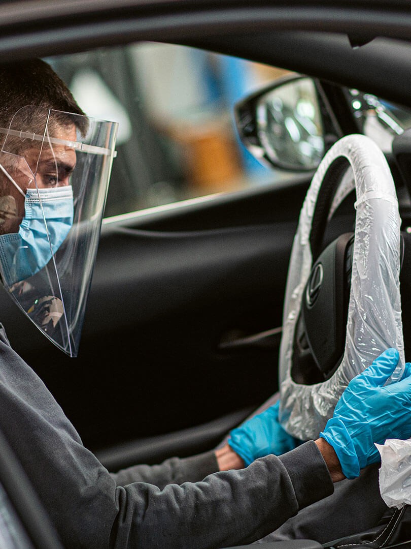 A Lexus staff member sitting inside a Lexus wearing personal protective equipment